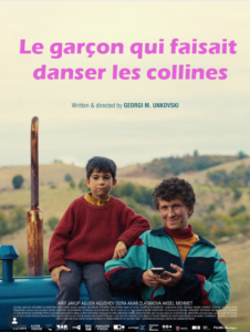 Affiche du film Le garçon qui faisait danser les collines, un garçon est assis sur un tracteur bleu et son père se tient debout à côté. En arrière plan des collines.